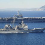 Naval warship escorting commercial cargo vessel in the Red Sea amid rising maritime tensions